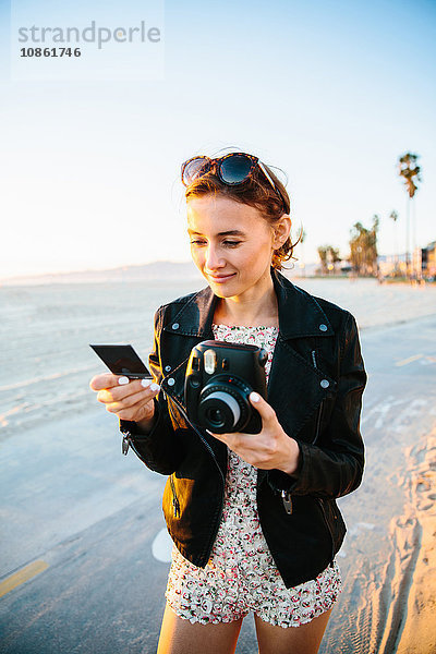 Junge Frau betrachtet Sofortbild am Strand  Venice Beach  Kalifornien  USA