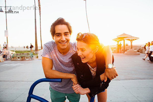 Porträt eines glücklichen jungen Paares  das sich an eine Fahrradskulptur an der Küste lehnt  Venice Beach  Kalifornien  USA