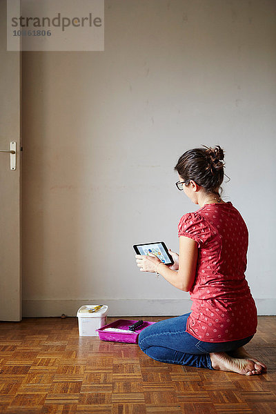 Frau kniend neben Dekorationsgeräten  Blick auf digitales Tablett  Rückansicht