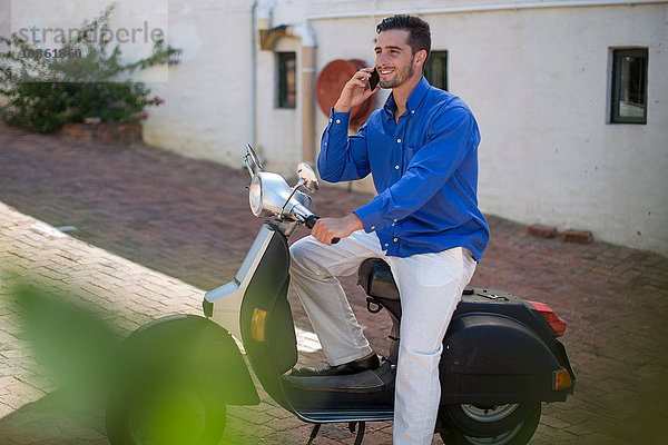 Junger Mann auf Moped chattet auf Smartphone in der Stadt