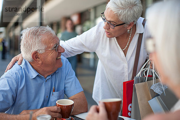 Shopperin begrüßt älteren Mann im Straßencafé