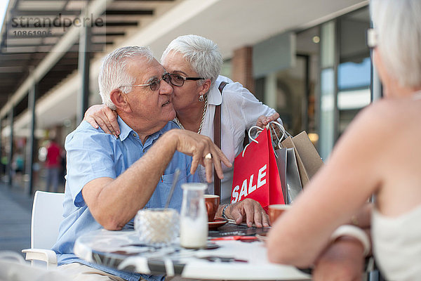 Shopperin küsst älteren Mann im Straßencafé auf die Wange