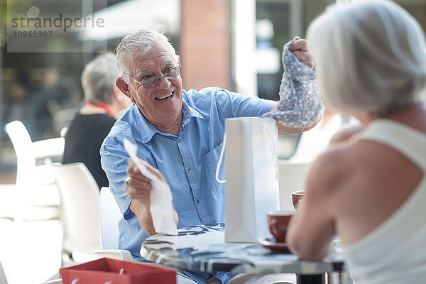 Älterer Mann entfernt Schal aus Einkaufstasche für Frau im Straßencafé