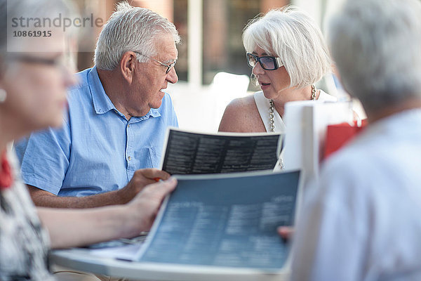Älterer Mann und reifere Frauen lesen Speisekarten im Straßencafé