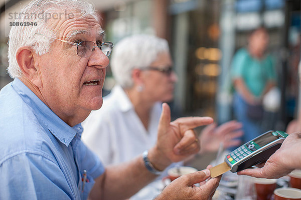 Ältere Freunde sitzen im Café  älterer Mann bezahlt Rechnung mit Kreditkarte