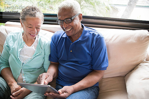 Älteres Ehepaar sitzt auf dem Sofa und benutzt ein digitales Tablett