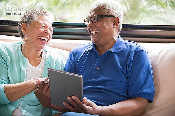 Älteres Ehepaar sitzt auf dem Sofa und benutzt ein digitales Tablett