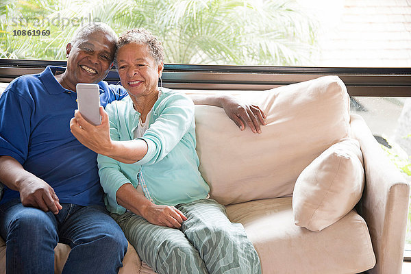 Älteres Ehepaar sitzt auf dem Sofa und macht ein Selbstporträt mit einem Smartphone