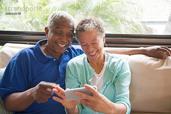 Älteres Ehepaar sitzt auf dem Sofa  schaut auf das Smartphone  lacht