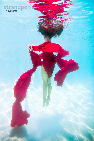 Frau in rotem Kleid  mit rotem Stoff drapiert  schwimmt unter Wasser