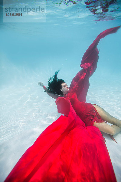 Frau in rotem Kleid  mit rotem Stoff drapiert  schwimmt unter Wasser