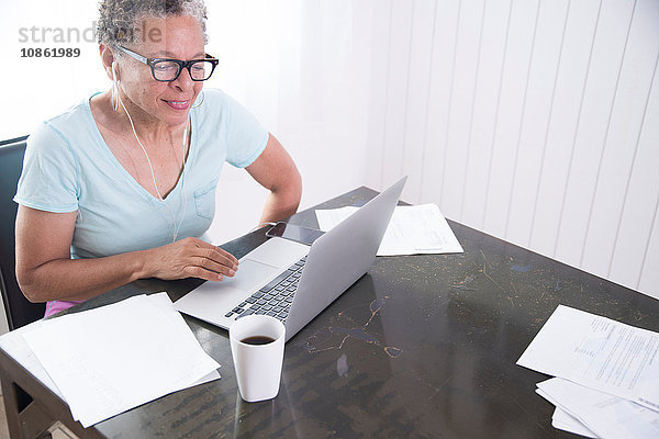 Ältere Frau am Tisch sitzend  mit Laptop  Papierkram auf dem Tisch