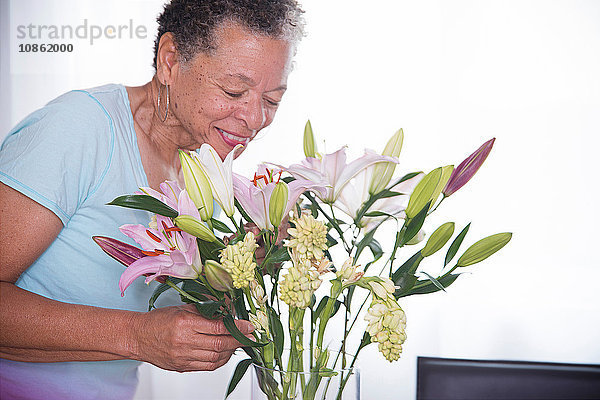 Ältere Frau riecht Vase mit Blumen und lächelt