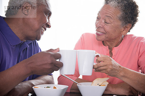 Älteres Ehepaar frühstückt gemeinsam  trinkt mit Kaffeetassen  lächelt