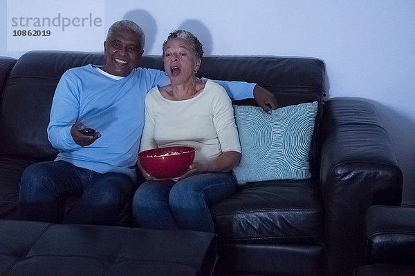 Älteres Ehepaar sitzt nachts auf dem Sofa  sieht fern  Frau hält eine Schüssel Popcorn