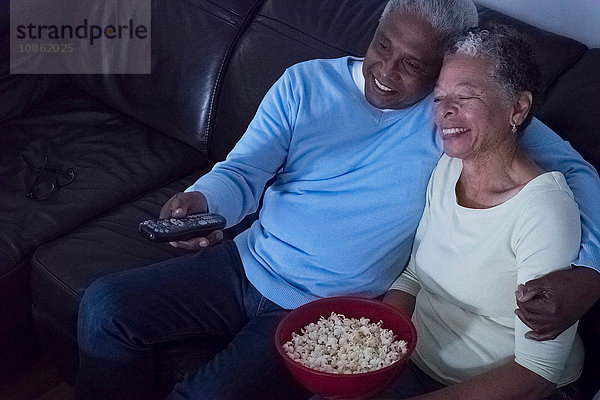 Älteres Ehepaar sitzt nachts auf dem Sofa  sieht fern  Frau hält eine Schüssel Popcorn