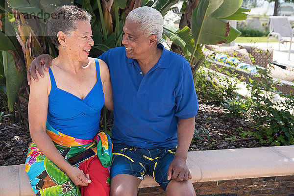 Älteres Ehepaar sitzt an der Wand  im Freien  von Angesicht zu Angesicht  lächelnd