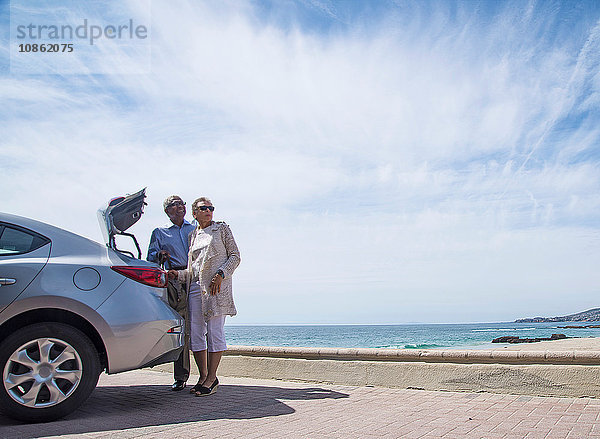 Älteres Ehepaar steht mit offenem Kofferraum neben dem Auto  in Strandnähe
