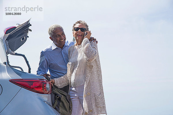 Älteres Ehepaar steht mit offenem Kofferraum neben dem Auto  Frau benutzt Smartphone