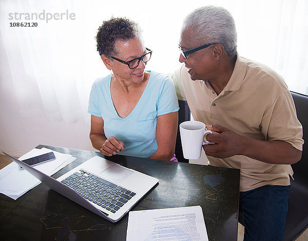 Älteres Ehepaar sitzt am Tisch  benutzt Laptop  Mann hält Kaffeetasse