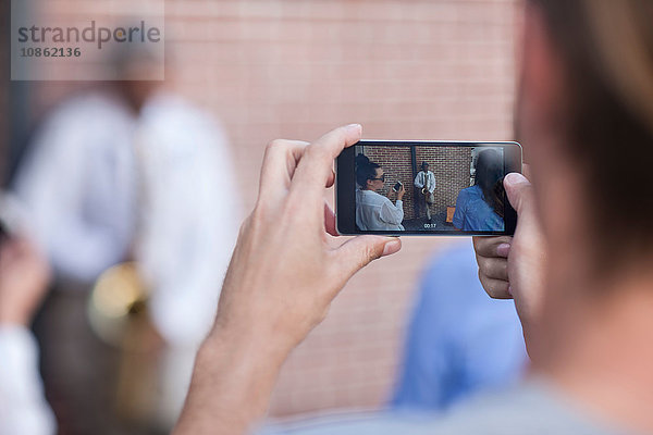 Fußgänger fotografiert einen Straßenmusikanten mit einem Smartphone