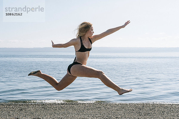 Teenager-Mädchen im Bikini  springend  in der Luft  am Strand