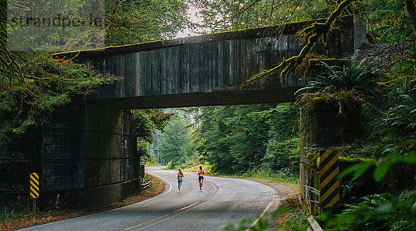 Junge Frau und jugendliches Mädchen rennen entlang einer Landstraße  Rückansicht