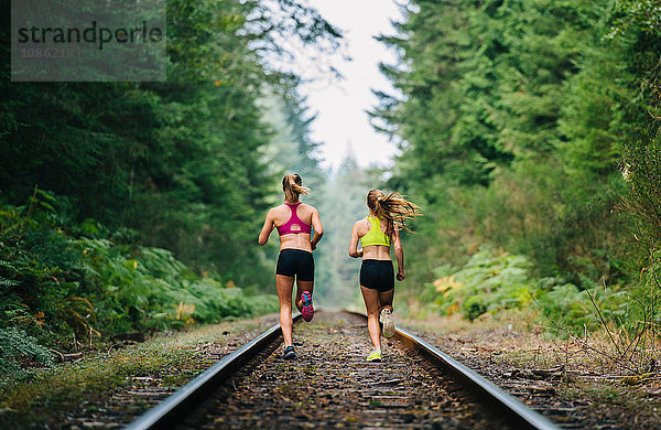 Junge Frau und junges Mädchen laufen auf einer ländlichen Zugstrecke  Rückansicht