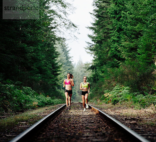 Junge Frau und junges Mädchen rennen auf ländlicher Bahnstrecke