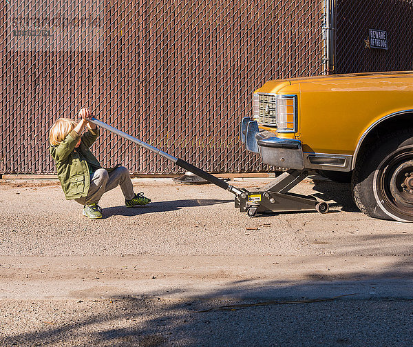 Junge benutzt Wagenheber zum Anheben eines Autos