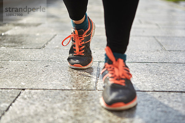 Beine einer Frau mit Laufschuhen auf dem Bürgersteig