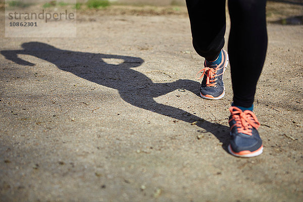 Schatten und Beine einer Frau mit Laufschuhen