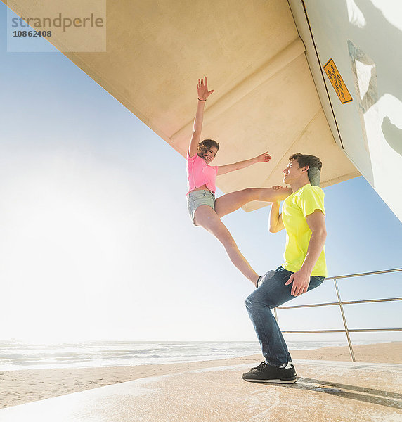 Paar übt Partner-Yoga auf dem Rettungsschwimmerturm am Strand