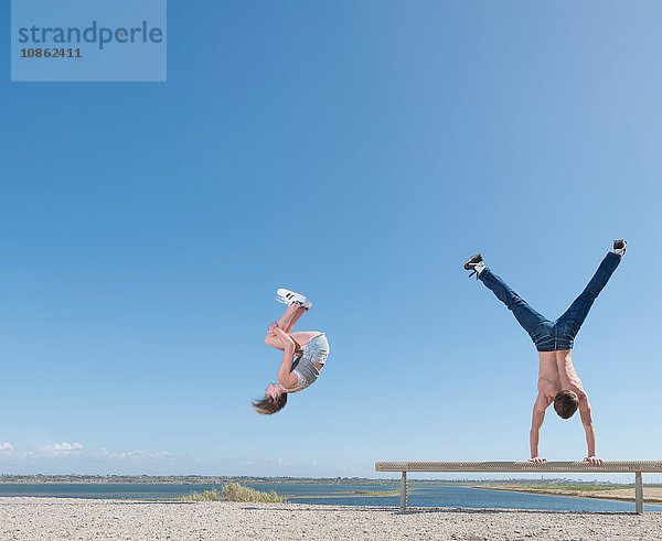 Mädchen beim Purzelbaum  Junge beim Handstand auf der Strandbank