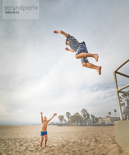 Junger Mann springt am Strand von Venice Beach  Kalifornien  USA  in die offenen Arme eines Jungen