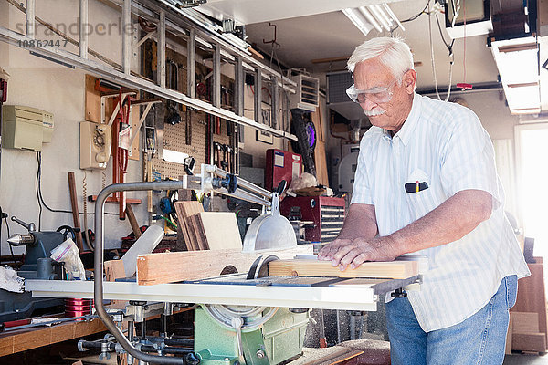Älterer Mann sägt Holzblock auf Kreissäge in Schreinerei