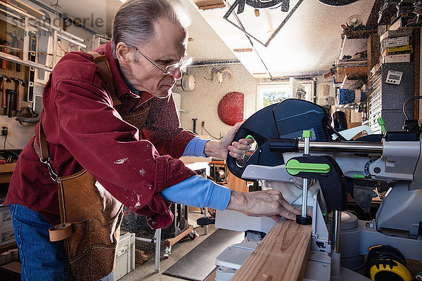 Älterer Mann sägt Holzblock in Schreinerei