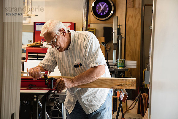 Älterer Mann platziert Holzblock auf Schreinerei-Ausrüstungswerkstatt