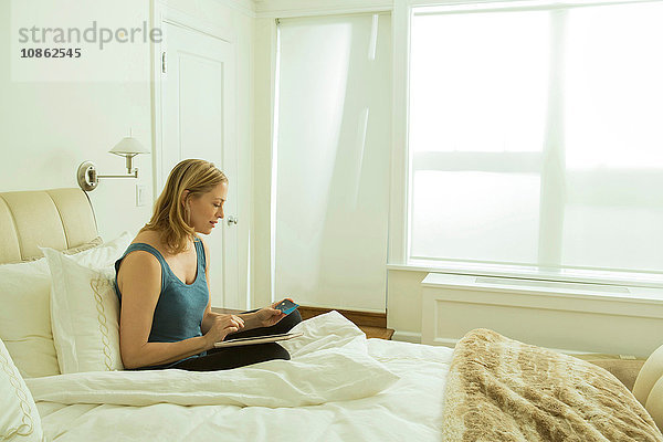 Frau sitzt im Bett und liest Update auf digitalem Tablet