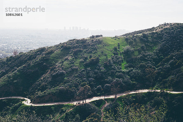 Erhöhte Ansicht einer kurvenreichen Straße und von Hügeln mit weit entfernter smogiger Stadtlandschaft  Los Angeles  Kalifornien  USA
