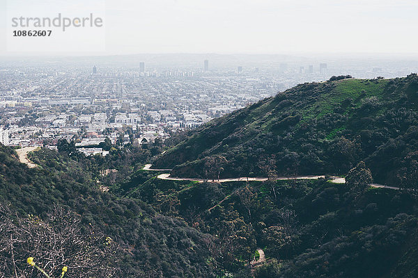 Erhöhte Aussicht auf Hügel und kurvenreiche Straße mit weit entfernter  smogiger Stadtlandschaft  Los Angeles  Kalifornien  USA