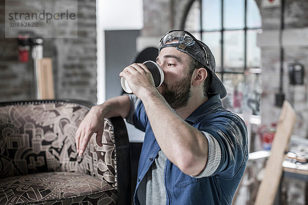 Arbeiter in Restaurierungswerkstatt für Antiquitäten trinkt Kaffee zum Mitnehmen