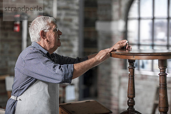 Leitender Handwerker inspiziert Tisch in Restaurierungswerkstatt für Antiquitäten