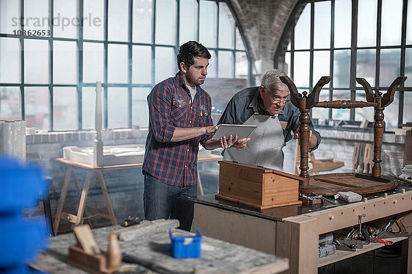 Auszubildender Handwerker mit digitalem Tablett in einer Restaurierungswerkstatt für Antiquitäten