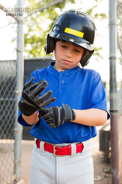 Junge zieht auf dem Baseballfeld Baseballhandschuhe an