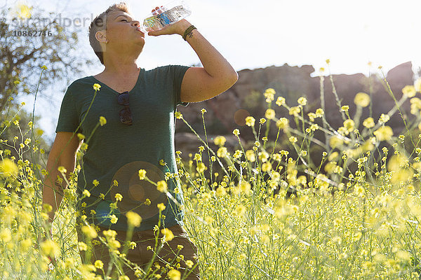 Frau in Wildblumenwiese trinkt Wasser aus der Flasche