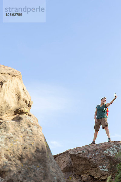 Wanderfrau steht auf Felsen und benutzt Smartphone zur Selbsthilfe