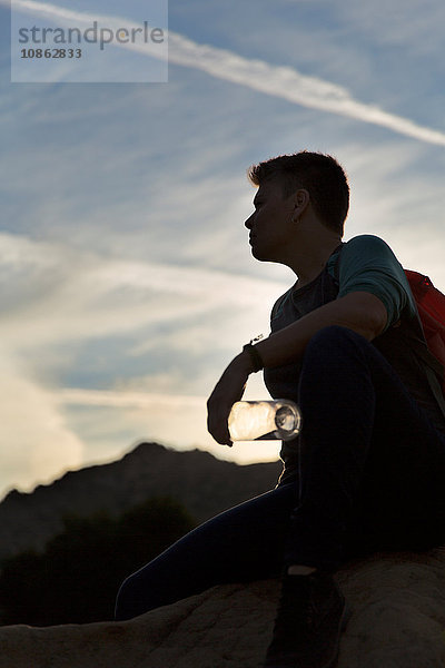 Silhouette einer Wanderin  die sitzend eine Wasserflasche hält und wegschaut