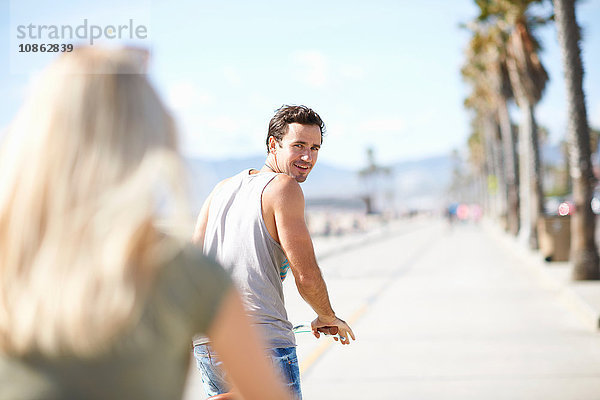 Mann blickt am Venice Beach  Los Angeles  Kalifornien  USA  beim Radfahren auf seine Freundin zurück