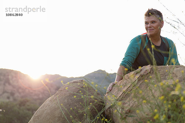Wanderfrau sitzt auf Felsen und schaut lächelnd weg